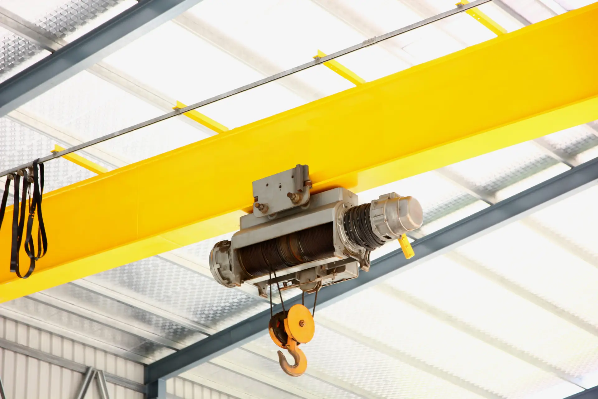 electric overhead crane install on yellow metal beam in warehouse. dictribution centers use cranes to move large quantities of heavy goods at once
