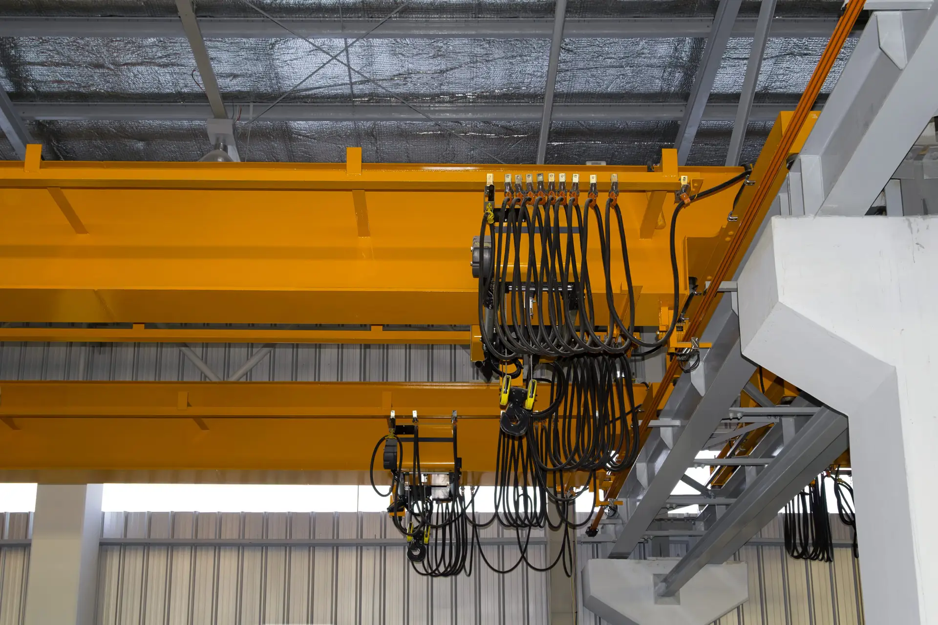 Overhead crane in factory or warehouse. Industrial machine or lifting equipment with hoist, hook and wire rope on beam girder structure for manufacturing production and freight shipping transport.