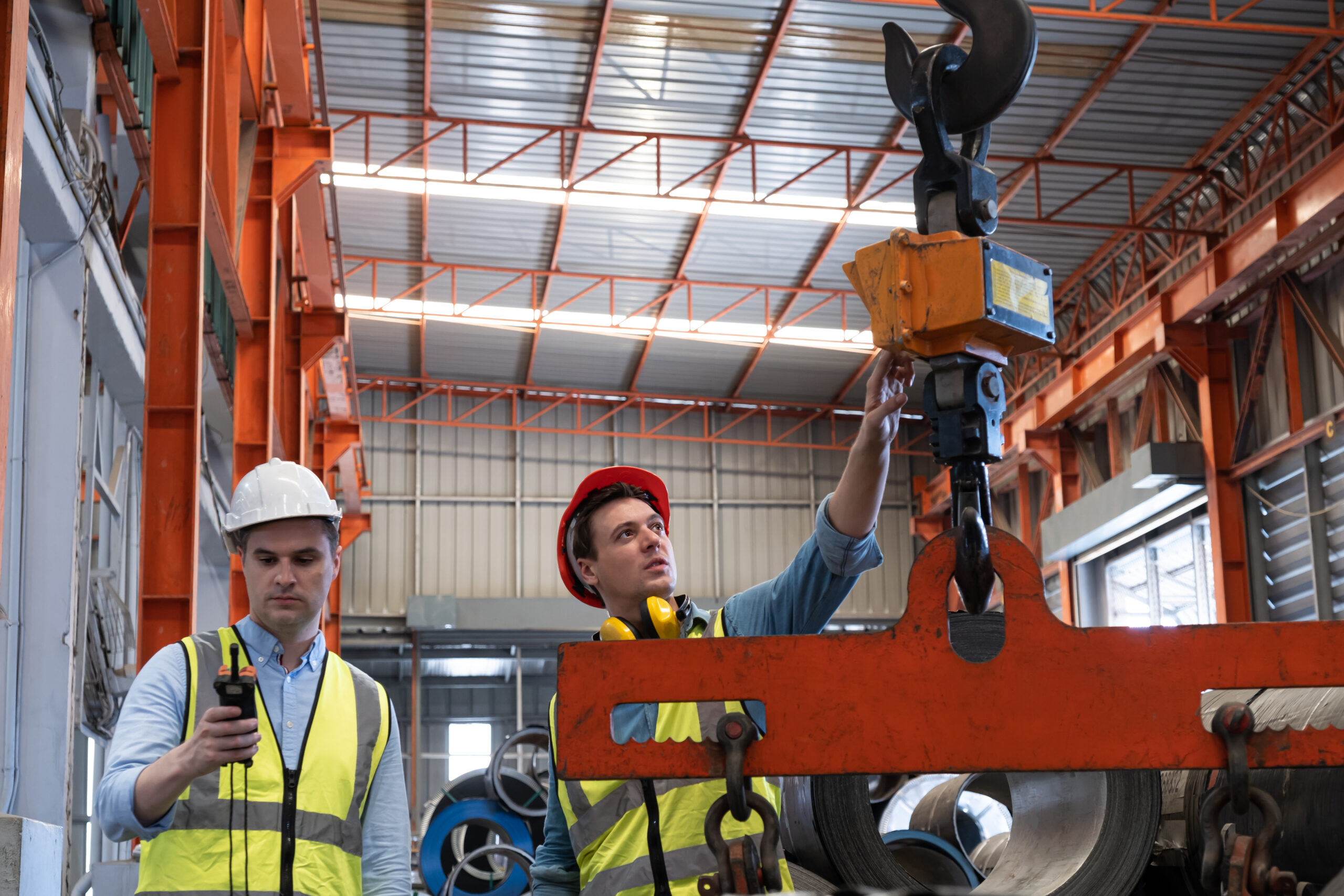 Selective focus at Caucasian men mechanical engineer, wearing safety equipment. While doing machine maintenance and safety control inside of factory area. With blurred background of heavy machine.