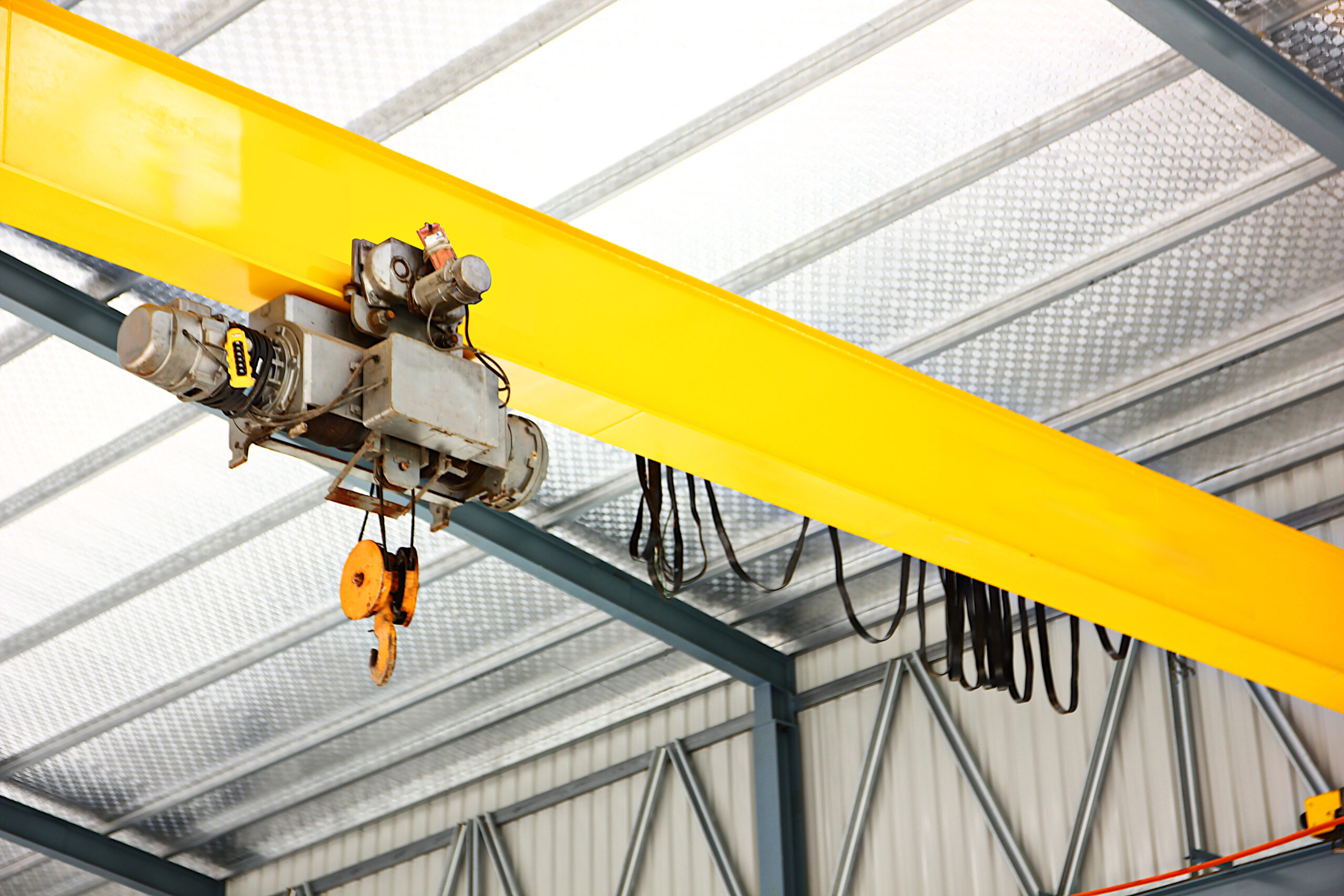 electric overhead crane install on yellow metal beam in warehouse. dictribution centers use cranes to move large quantities of heavy goods at once